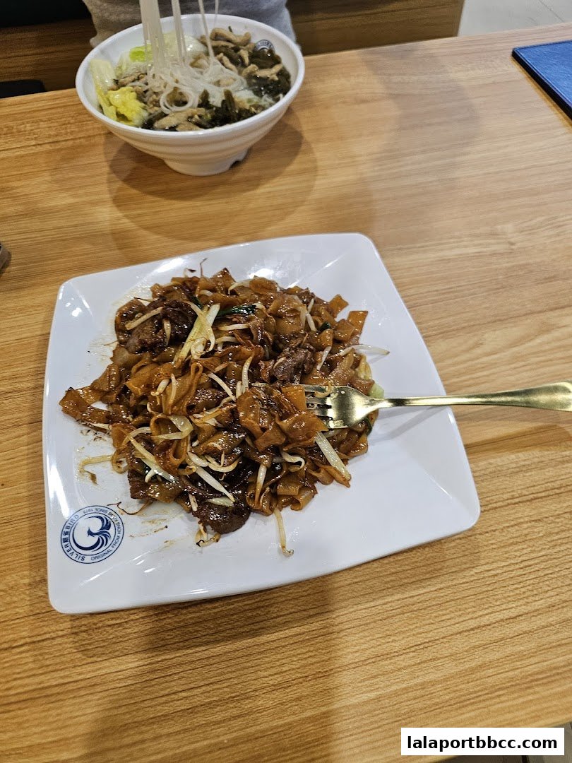 A plate of stir-fried noodles with beef and bean sprouts, and a bowl of soup with noodles and vegetables.
