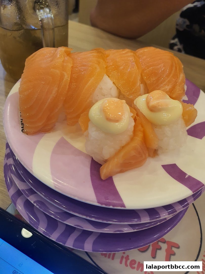 A close-up of salmon sushi on plates with a drink in the background.