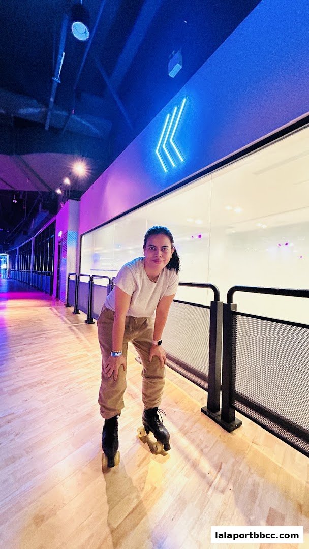 A woman wearing roller skates poses in a brightly lit roller skating rink with neon lights.