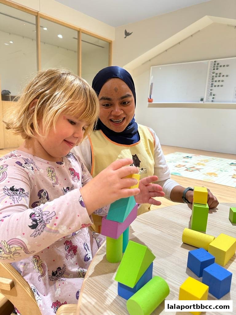 A child and caregiver happily build with colorful blocks at a table.
