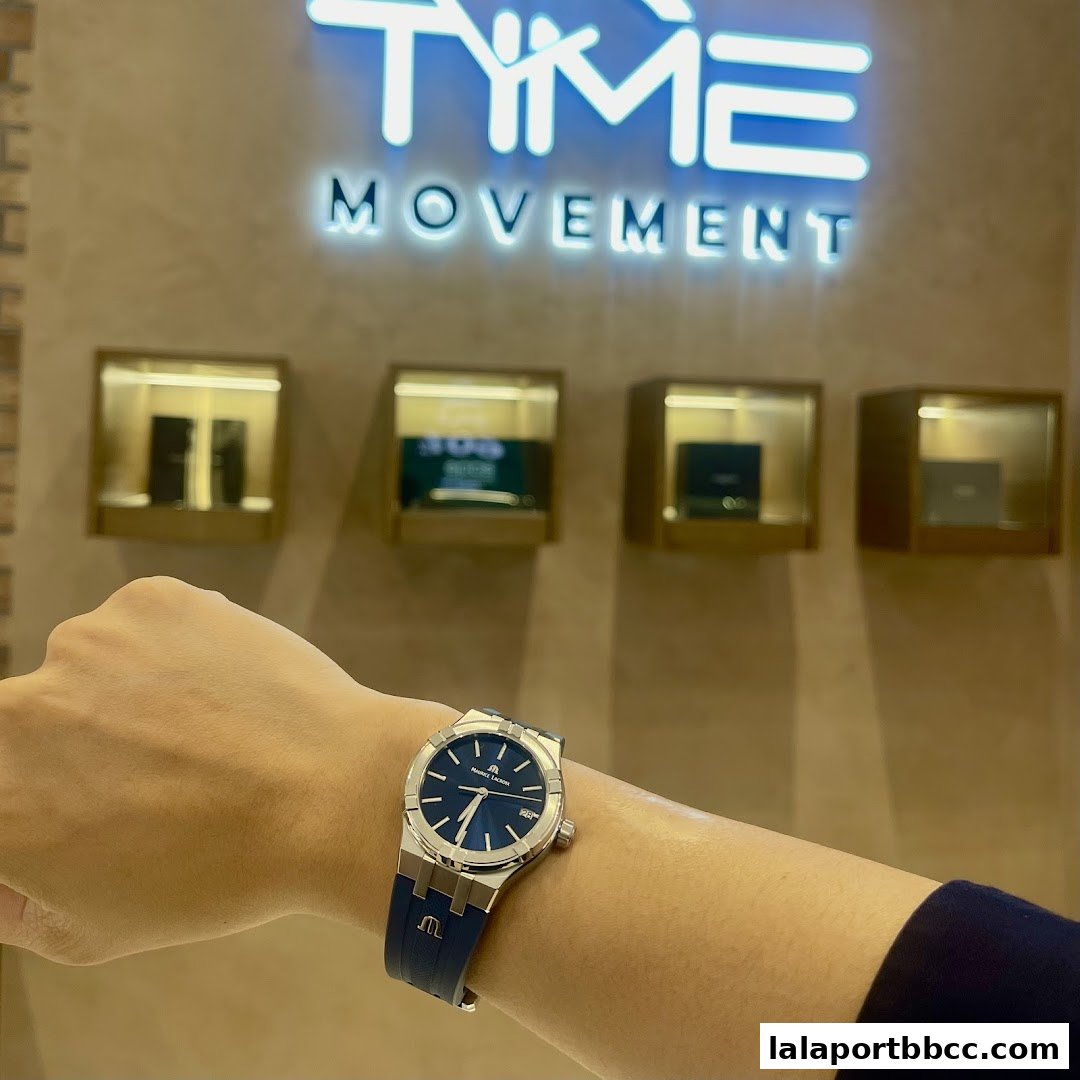 A person wearing a blue-faced watch with a blue strap in front of the Time Movement store logo.