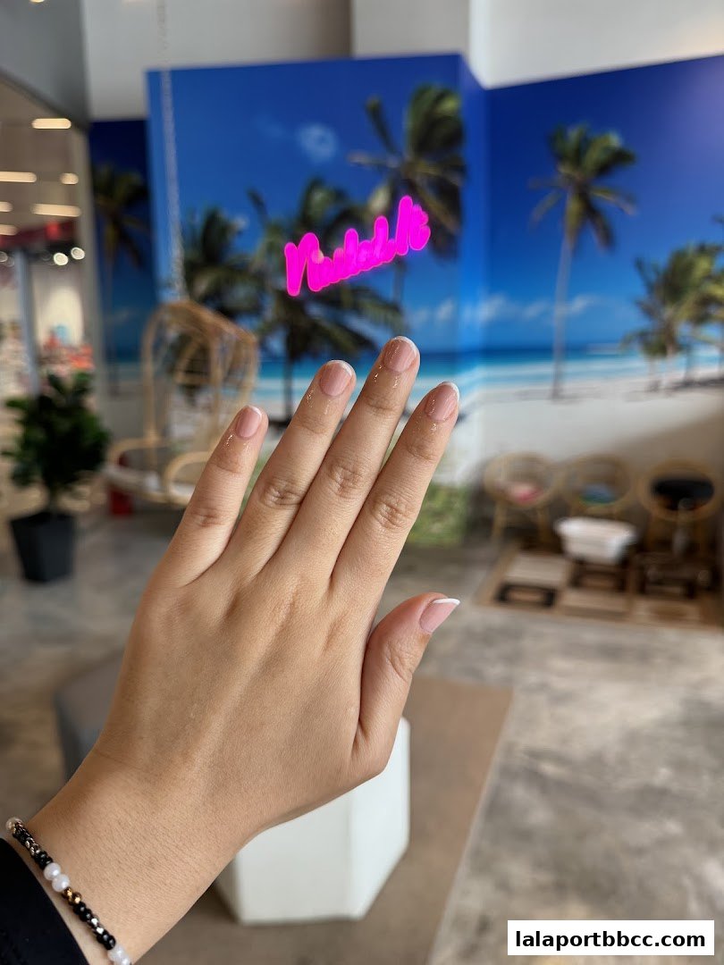 A hand with a fresh French manicure is shown in front of a tropical beach mural.