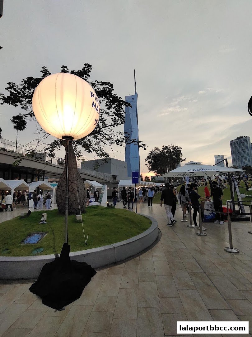 An outdoor event with people browsing stalls under a cloudy sky.