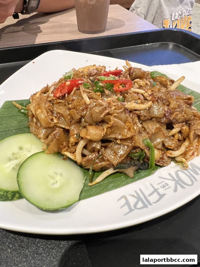 A plate of stir-fried noodles with chili, green onions, and cucumber slices.