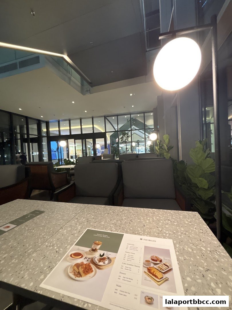 A menu from Padi Malaya restaurant is placed on a table with comfortable seating in the background.