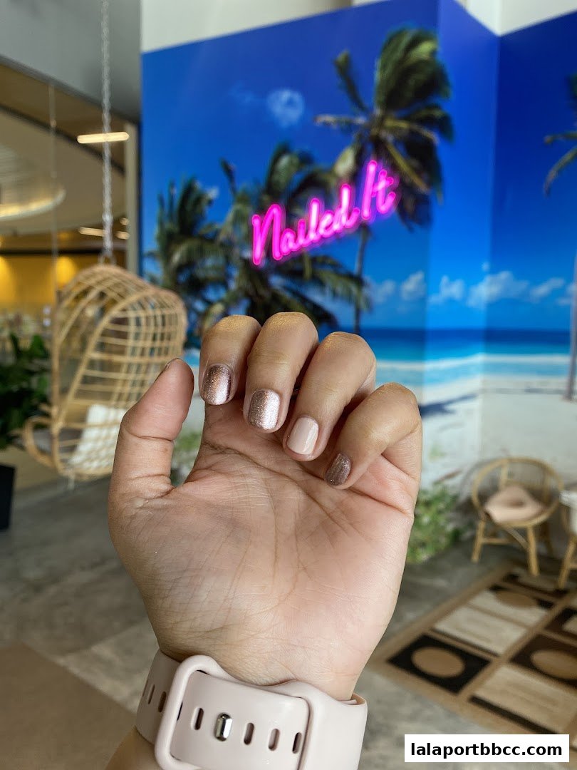 A hand with a fresh manicure in front of a tropical-themed wall with neon signage.