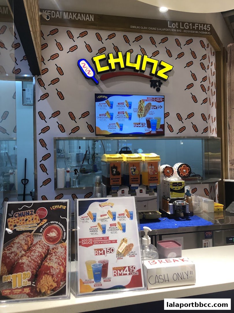 A food stall counter with a menu displaying corn dogs and drinks, and a sign indicating cash only.