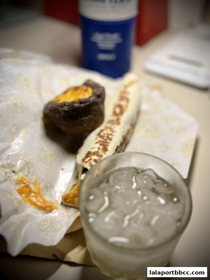 A close-up of a kebab wrap and a small pastry with a glass of iced drink.