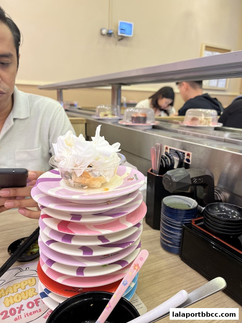A stack of colorful sushi plates with food remnants and a person holding a phone.