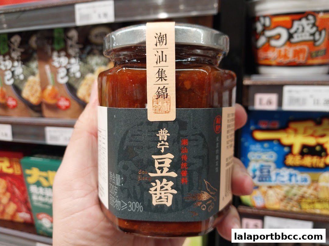 A hand holds a jar of fermented bean paste in a grocery store aisle.