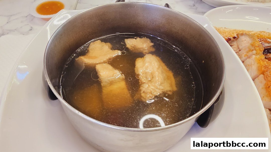 A close-up of a pot of savory broth with chunks of meat, served with a side of chili sauce.