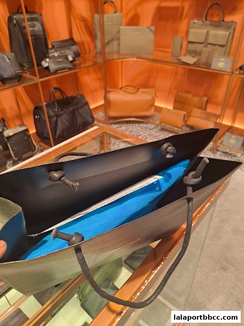 A shopping bag with a blue item inside, displayed in a store with leather goods.