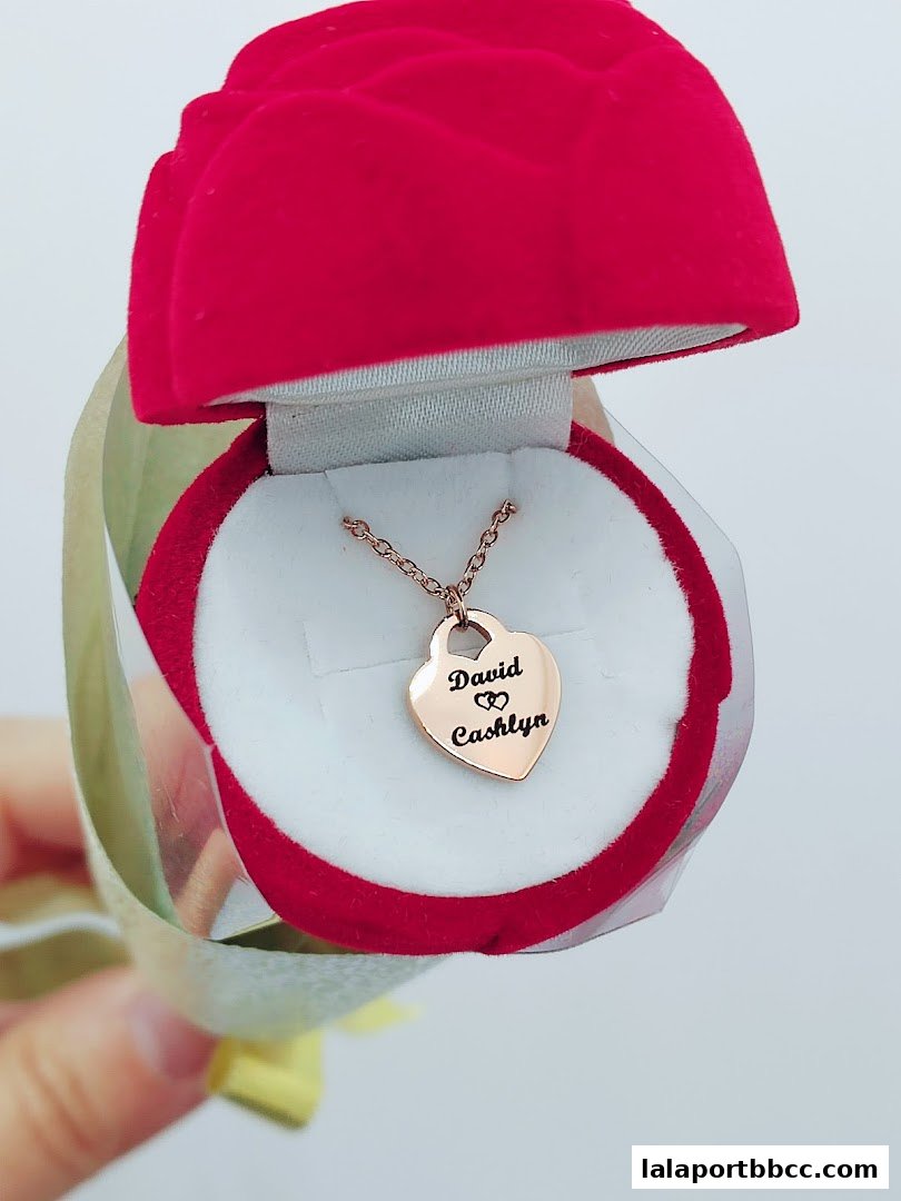 A rose-shaped jewelry box holds a personalized heart necklace with names engraved.