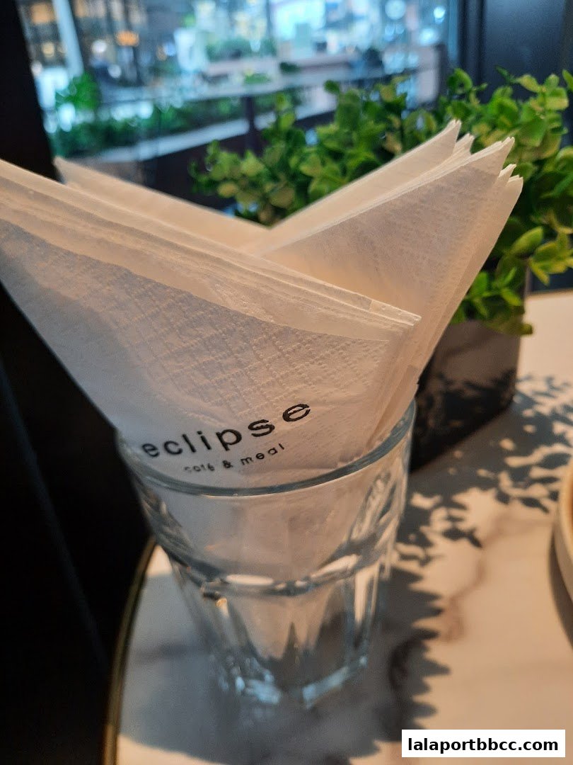 Napkins with the 'eclipse cafe & meal' logo in a glass, with plants and a blurred background.