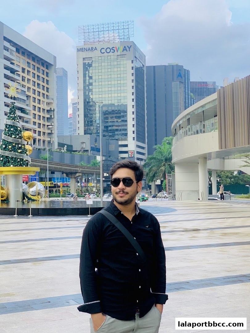 A man stands in front of a modern cityscape with tall buildings and a Christmas tree.