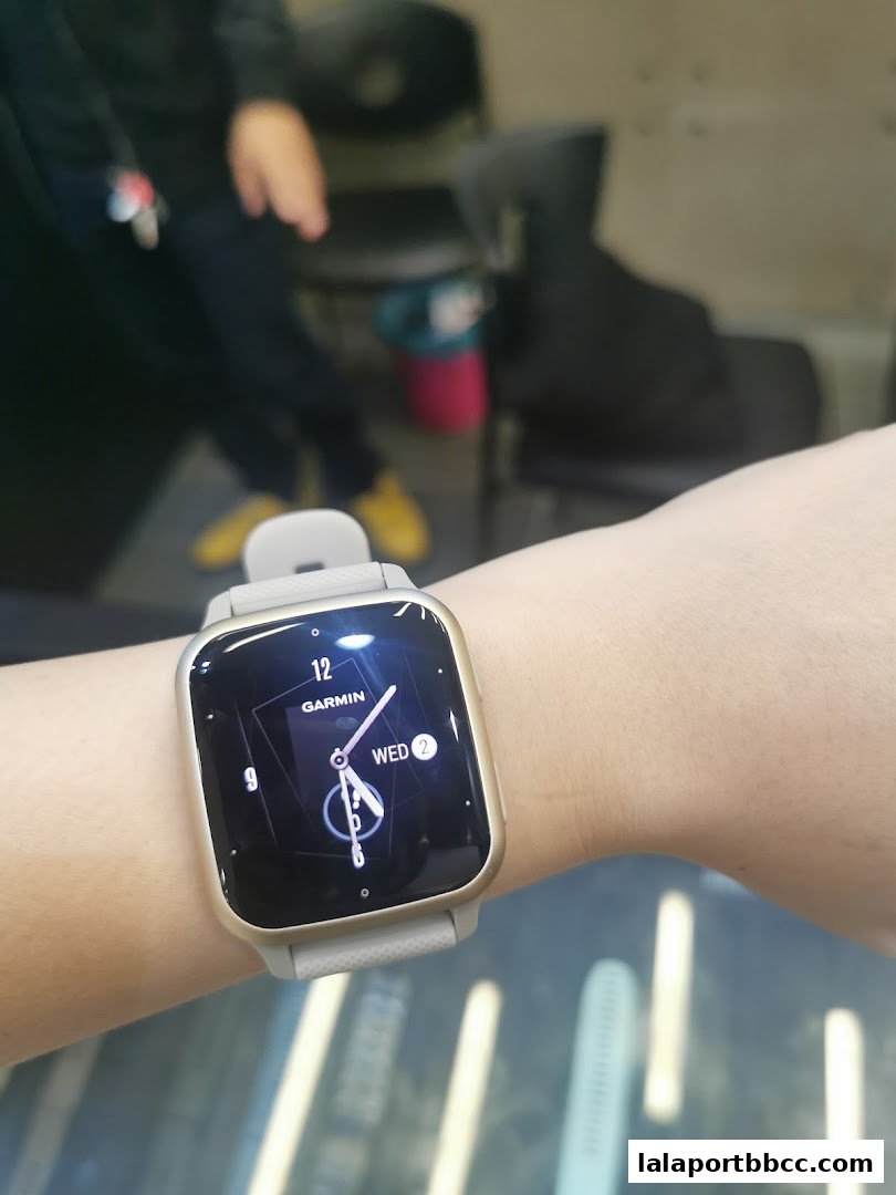 A person wearing a Garmin smartwatch with a gold bezel and a light grey strap.