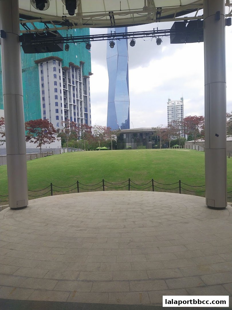 View of a park with modern buildings and a stage area.