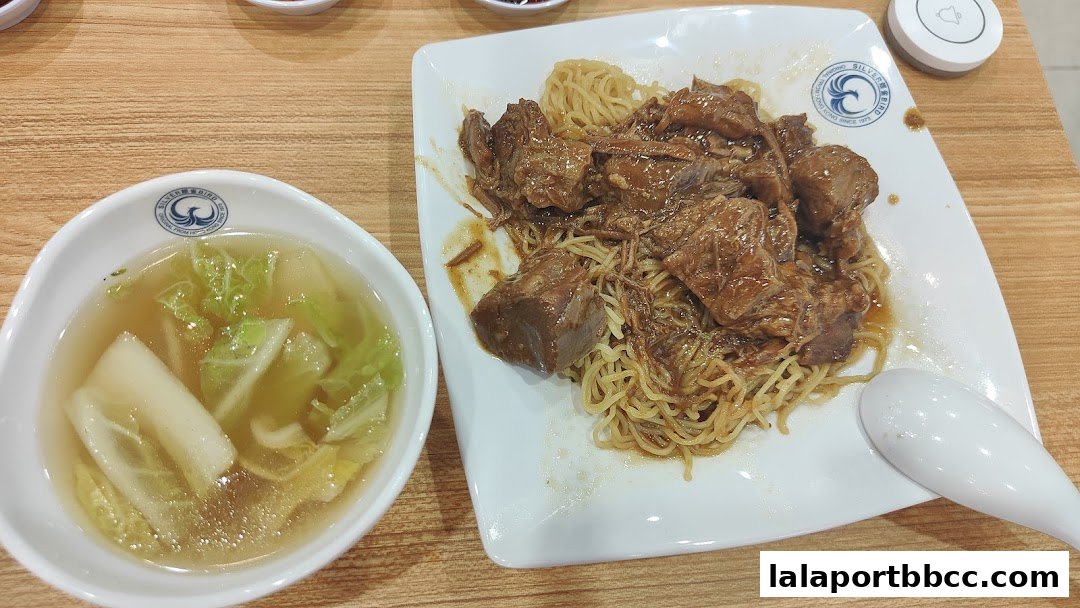 A plate of braised beef noodles with a side of clear soup with vegetables.