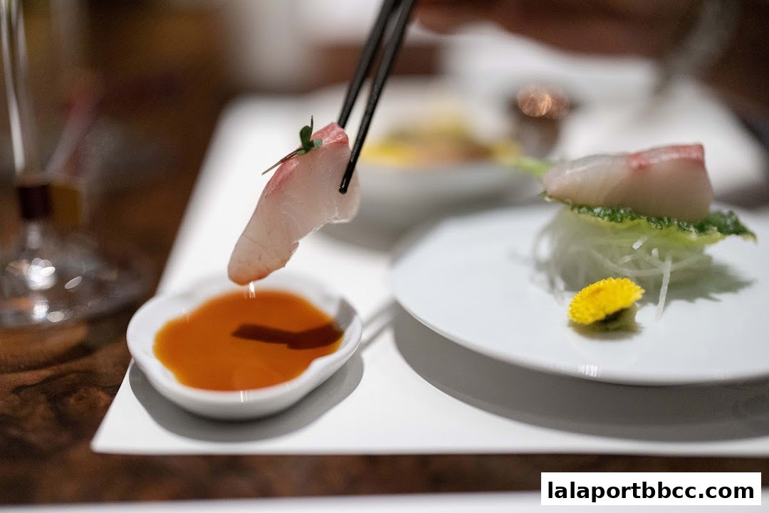 A close-up of fresh sashimi being dipped into soy sauce with chopsticks.