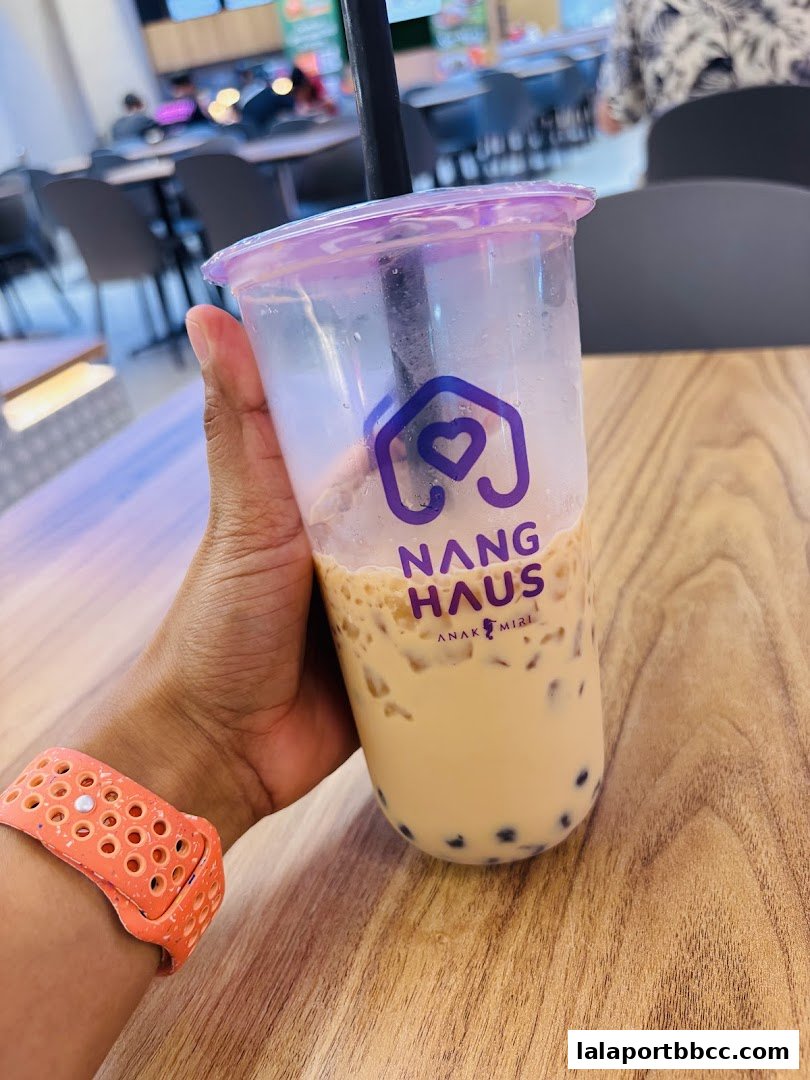 A hand holds a bubble tea with the Nang Haus logo, in a casual dining setting.