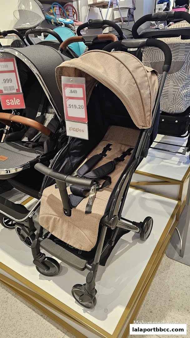 A close-up view of a beige baby stroller with safety straps and price tags.