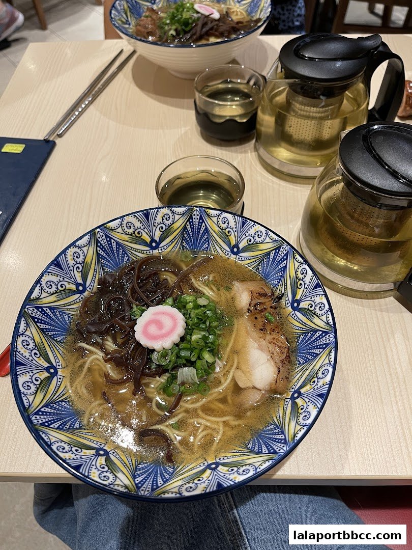 A close-up of a delicious bowl of ramen with pork, noodles, and toppings, served with tea.