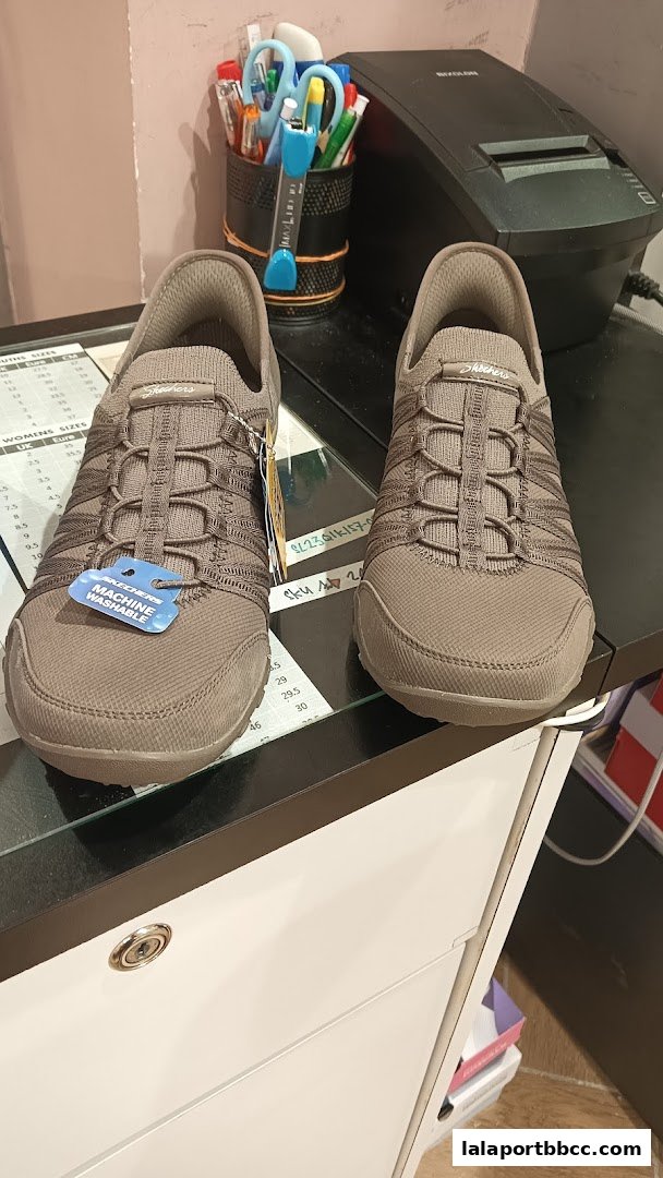 A pair of Skechers shoes displayed on a counter with a receipt printer and office supplies.