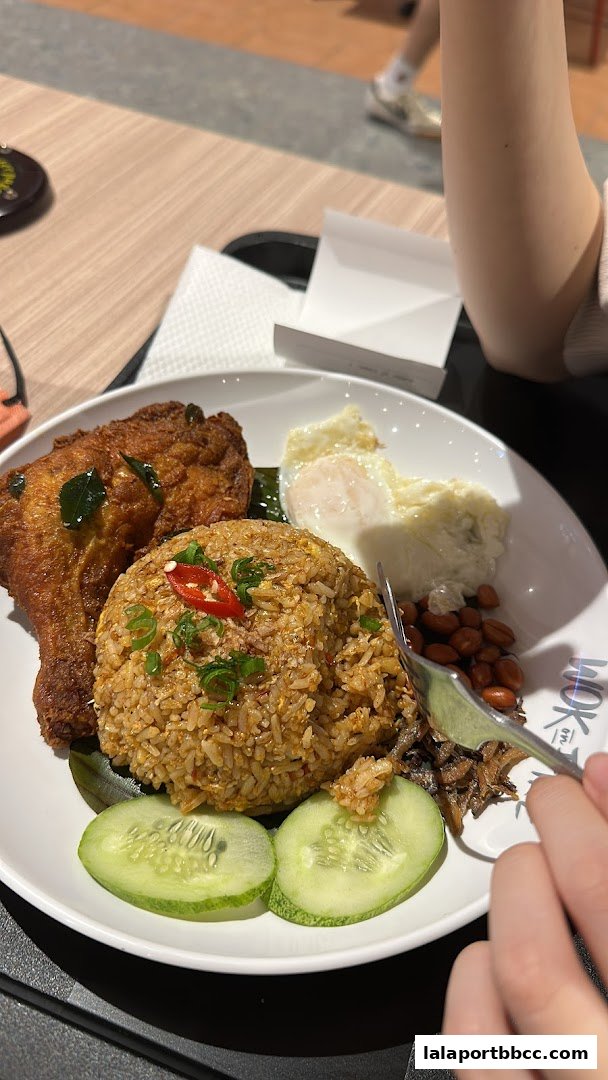 A plate of Nasi Lemak with fried chicken, fried rice, egg, peanuts, and cucumber.