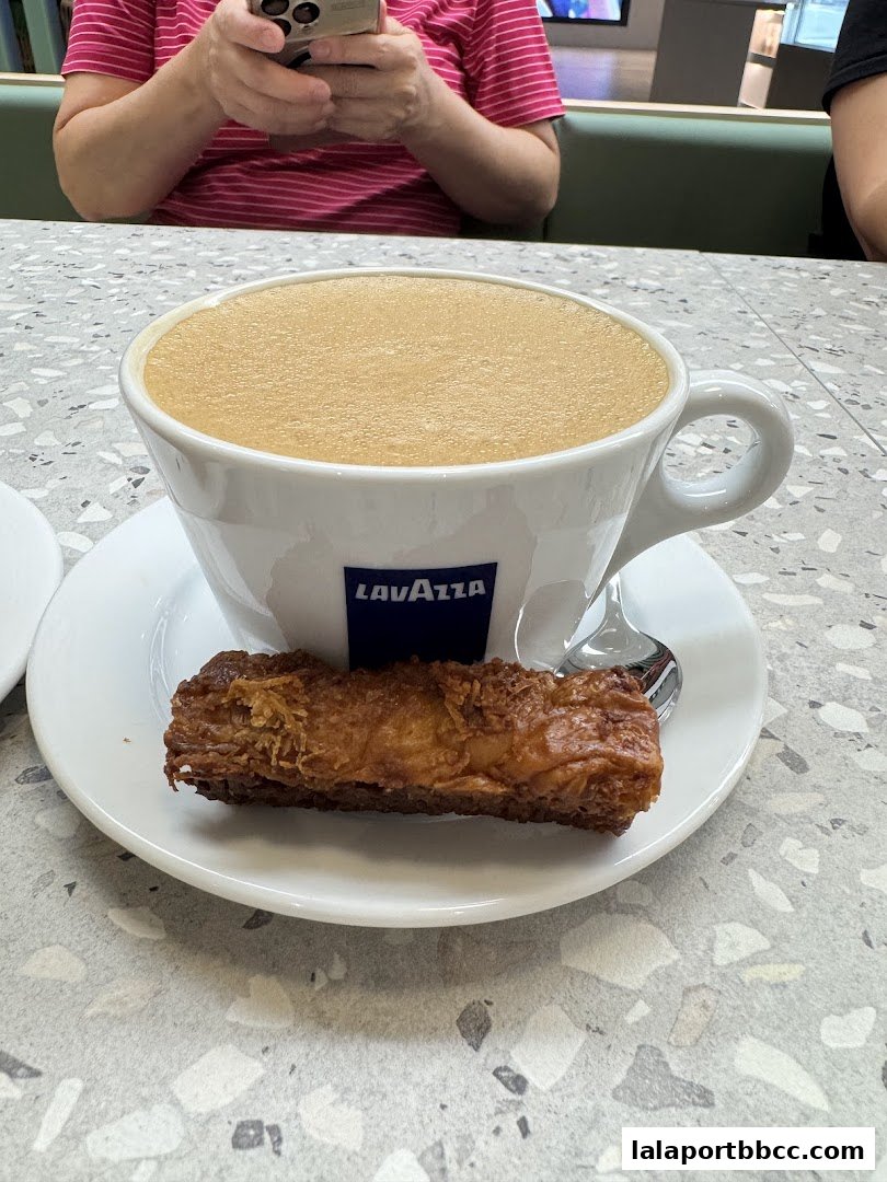 A close-up of a coffee with a pastry on a saucer, served at a cafe.