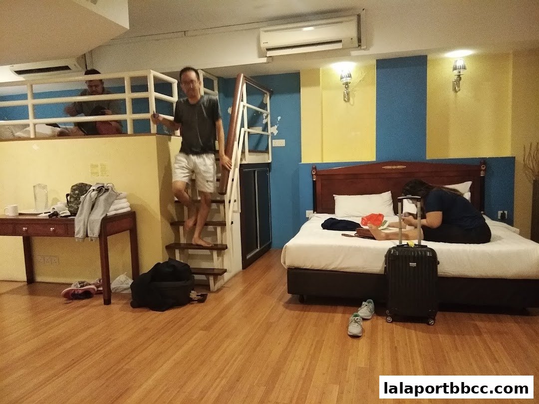 People in a hotel room with a loft, bed, and stairs.
