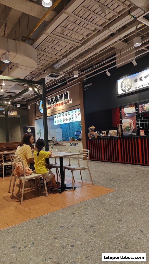 Two people sit at a table in front of a food stall with a menu displayed.