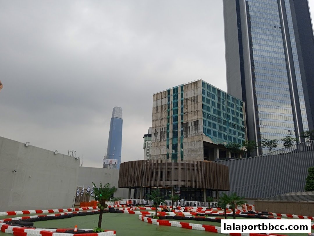 An outdoor go-kart track with a modern building and skyscrapers in the background.