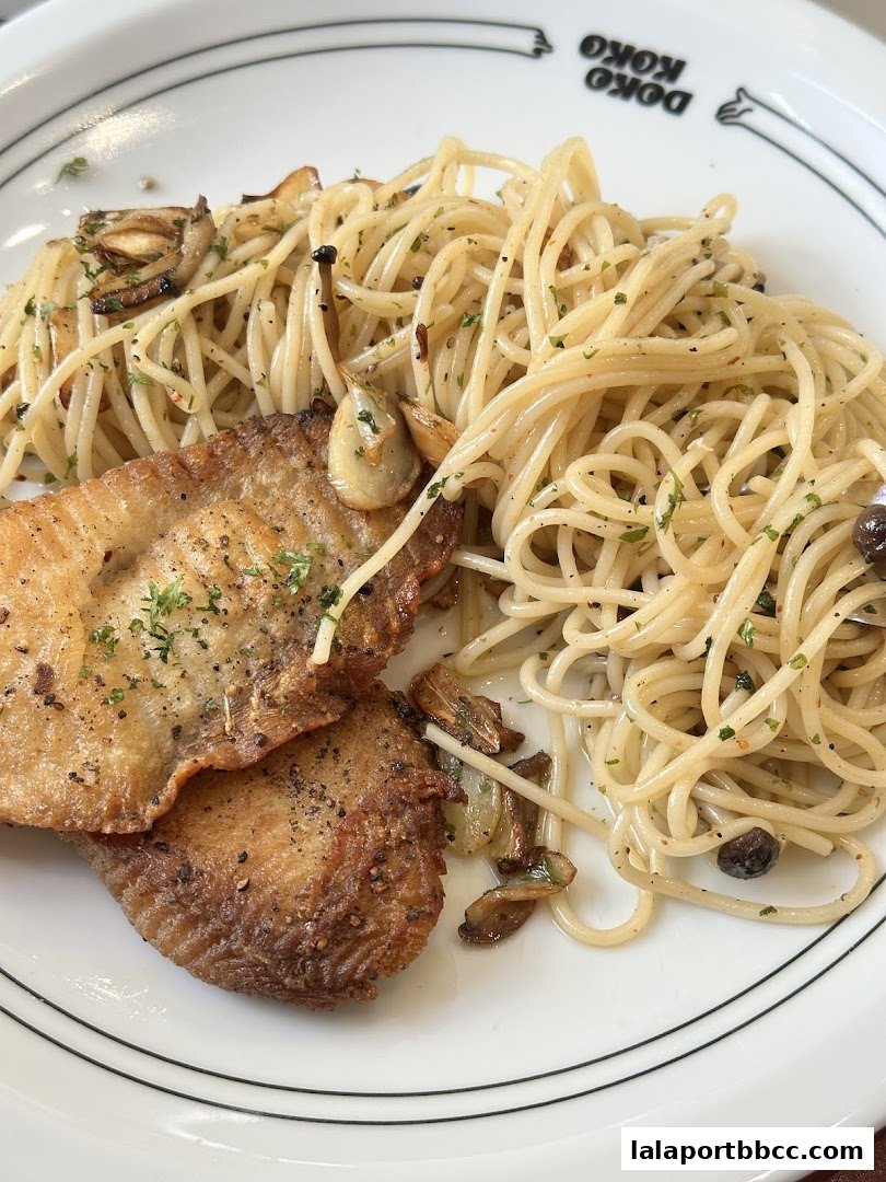 A plate of spaghetti with fried fish and garlic, garnished with herbs.