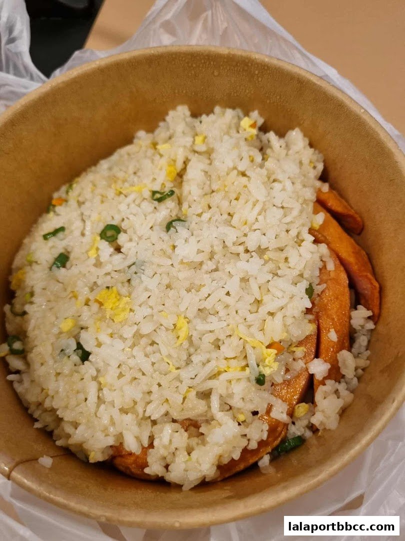 A close-up of a takeout container filled with fried rice and sliced meat.