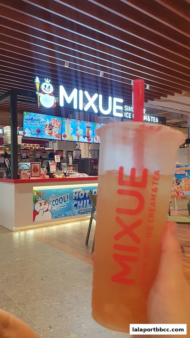 A person holds a MIXUE drink in front of the MIXUE ice cream and tea shop.