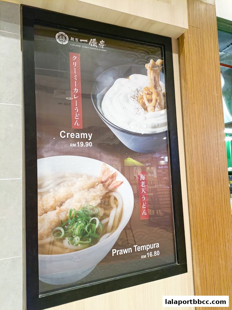 A menu board displays two Japanese noodle dishes: Creamy Curry Udon and Prawn Tempura Udon.