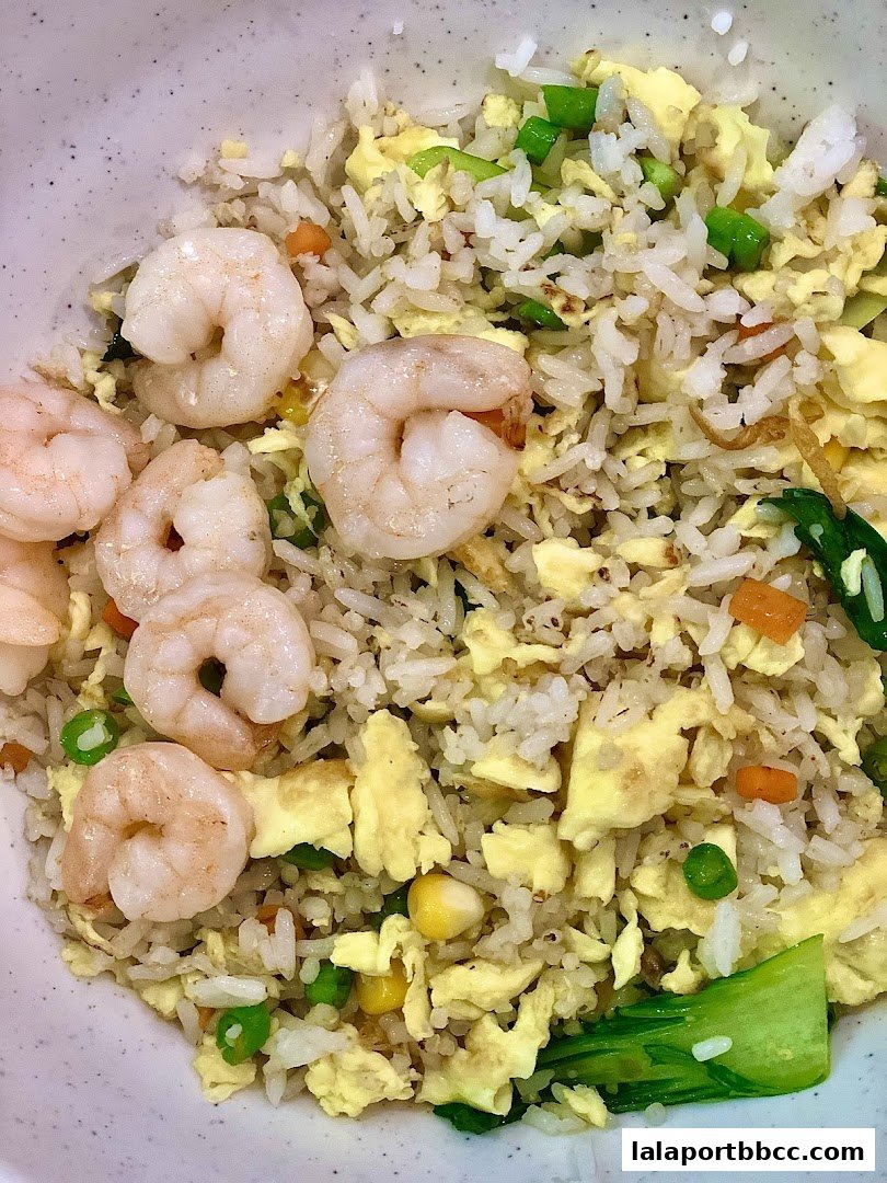 A close-up shot of a bowl of shrimp fried rice with vegetables and scrambled eggs.