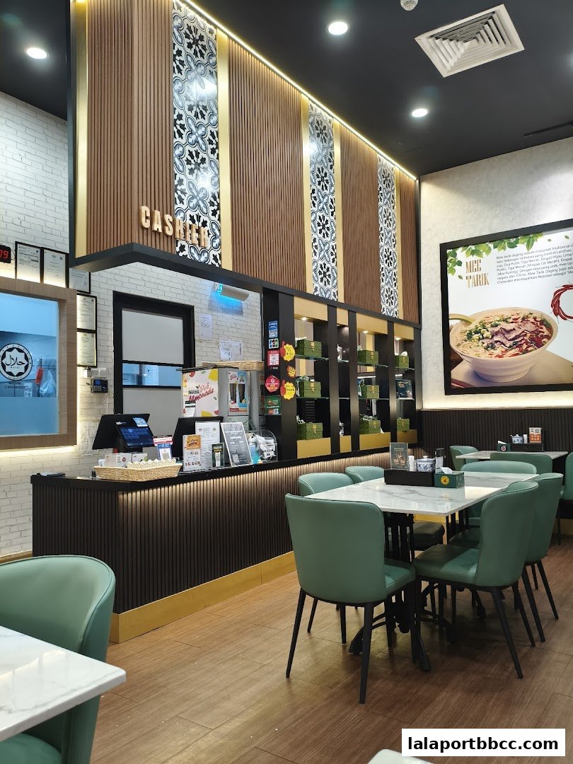 Interior of a modern restaurant with green chairs and tables, a cashier counter, and decorative wall panels.