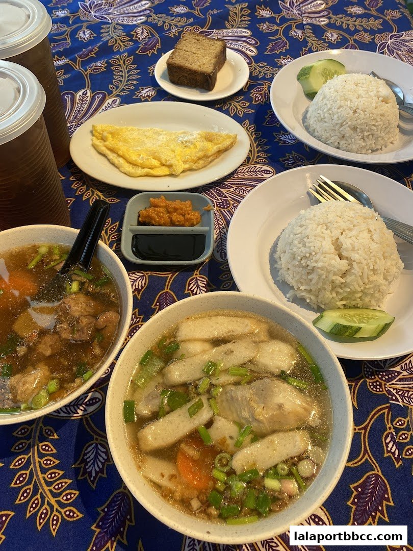 A table laden with delicious Malaysian dishes, including soup, rice, omelette, and drinks.