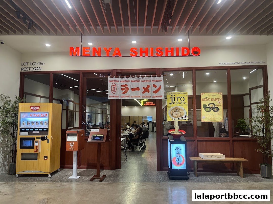 The entrance of Menya Shishido restaurant, featuring a vending machine, seating, and promotional posters.