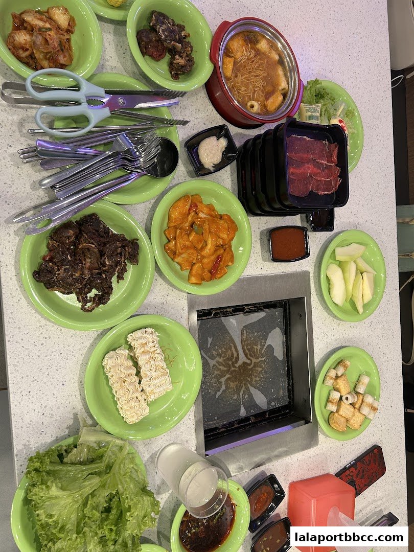A table filled with Korean BBQ ingredients, including meats, vegetables, and noodles.