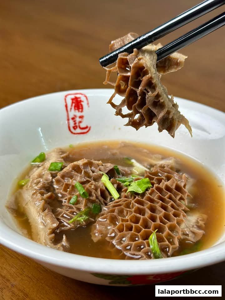 A close-up shot of a bowl of Hong Kong-style beef tripe noodles with broth and chopped scallions.