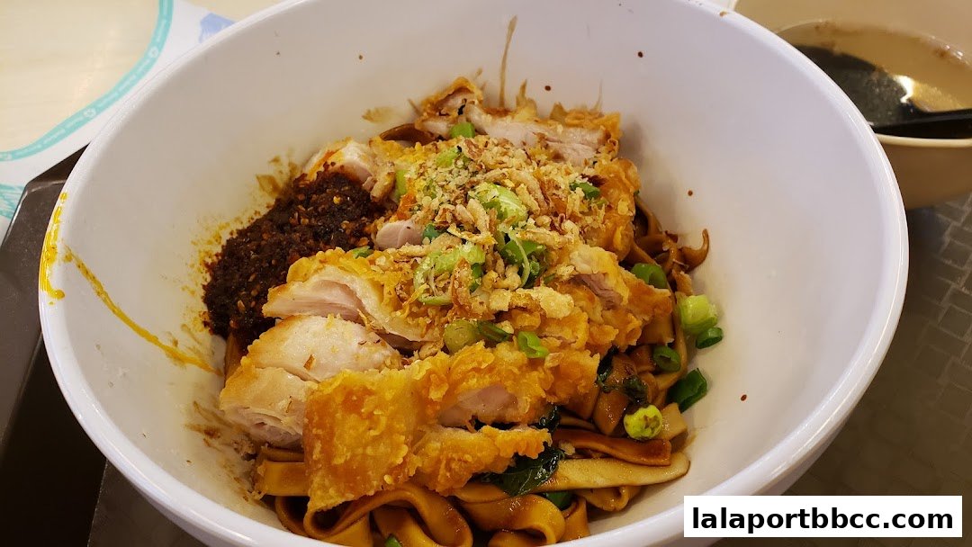 A close-up shot of a bowl of chili pan mee with fried chicken and spring onions.