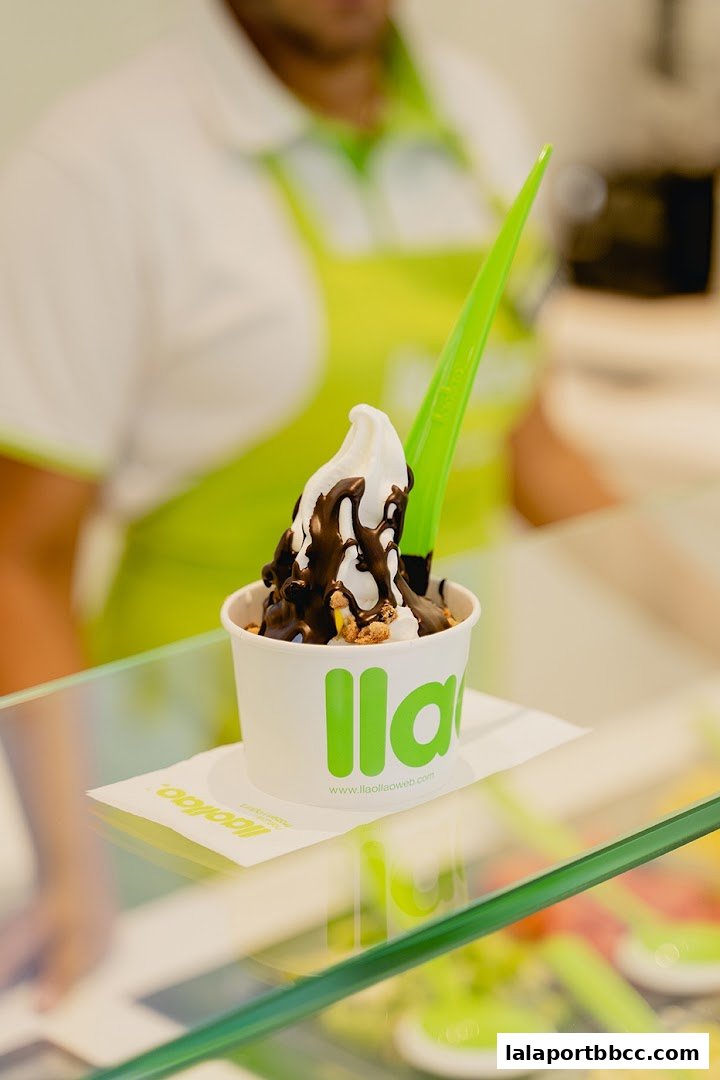 A cup of llaollao frozen yogurt with chocolate sauce and toppings, served by a staff member.