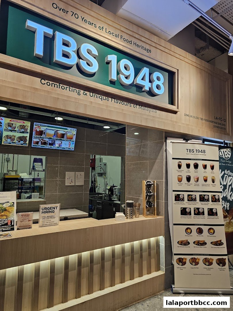 A food stall with a prominent sign for TBS 1948, featuring menu displays and a counter.