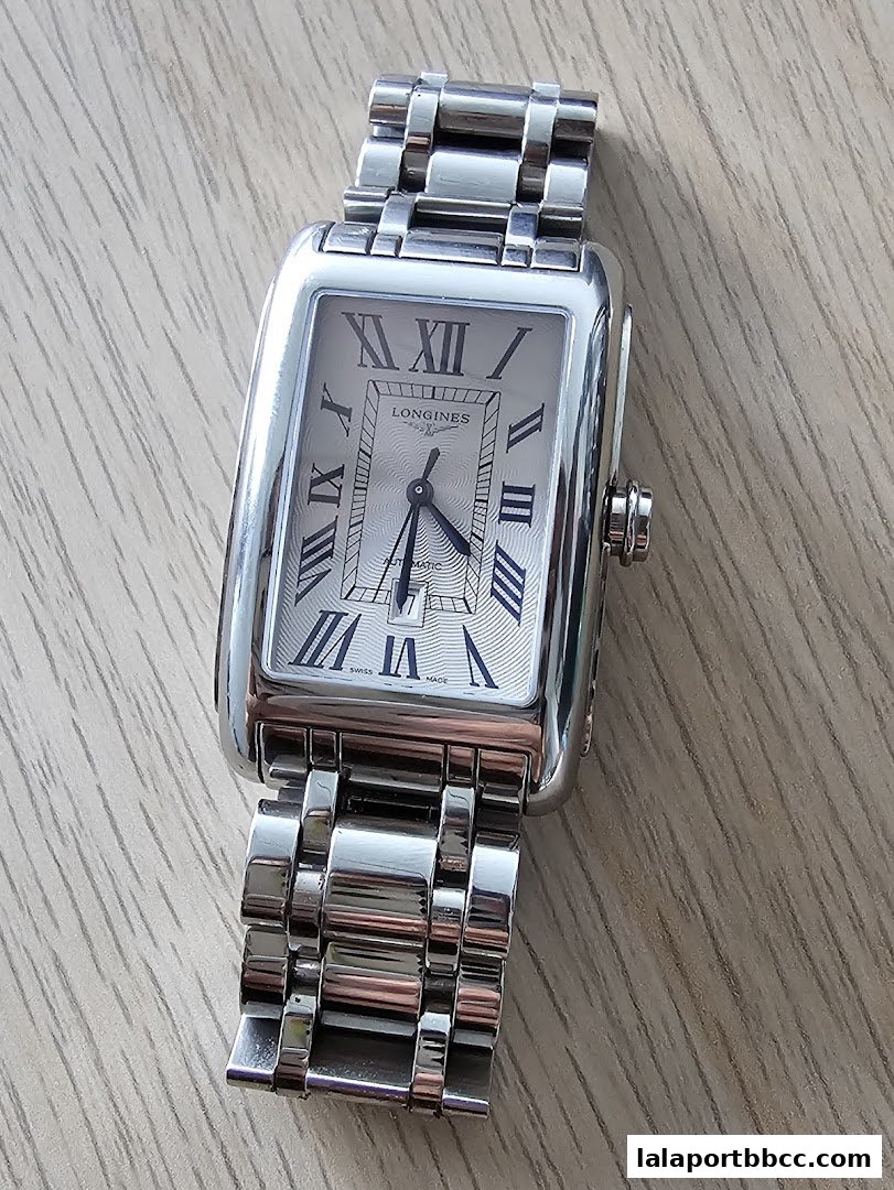 A close-up shot of a rectangular silver Longines watch with Roman numerals on a wooden surface.