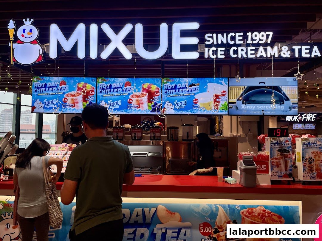 Customers ordering at a MIXUE ice cream and tea shop counter with digital menu displays.