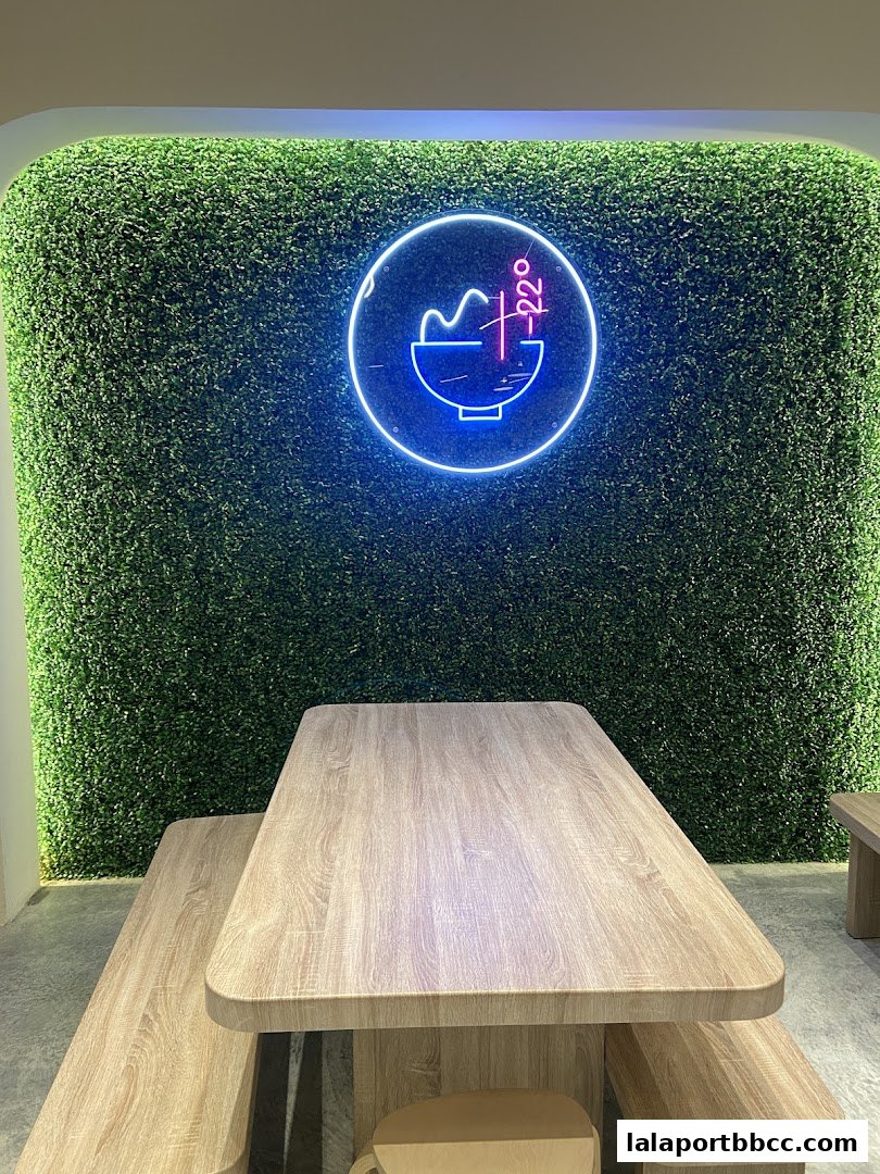 A modern dining area with wooden tables and benches against a green wall with a neon sign.