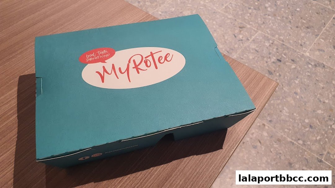 A teal takeout box with the MyRotee logo and slogan on a wooden surface.