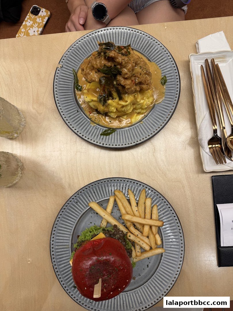 Two plates of food, one with a burger and fries, the other with a dish topped with meat and sauce.